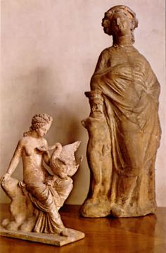 an old statue with a young boy next to it on a wooden table in front of a white wall