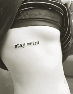 a woman's back with the words stay weird tattooed on her lower side leg