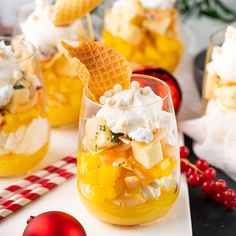 two glasses filled with fruit and ice cream on top of a white tray next to christmas decorations