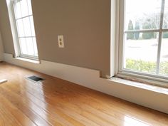 an empty room with hard wood floors and two windows in the wall, looking out onto a yard