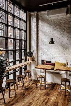 an empty restaurant with wooden tables and stools in front of large windows that look out onto the street