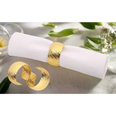 two gold toned rings on top of a napkin next to some wine glasses and flowers