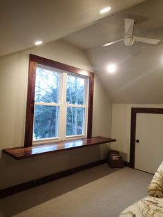 an empty room with a large window and ceiling fan in the corner, next to a bed