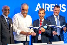 four men standing in front of a blue sign holding small model airplanes and smiling at the camera