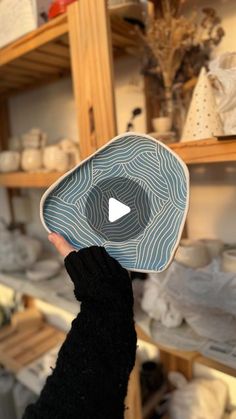 a person holding up a blue and white plate in front of shelves filled with cloths