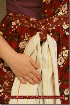 a woman wearing a red floral dress with her hand on the waist and holding onto an unbuttoned piece of cloth