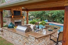 an outdoor kitchen with grill, sink and television on the wall next to pool area