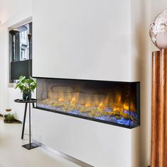 an electric fireplace in the middle of a room with white walls and floor to ceiling windows