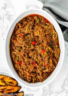 a white bowl filled with pulled pork and peppers next to two slices of bread on a marble surface