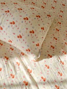 two pillows sitting next to each other on top of a bed covered in white and orange flowers