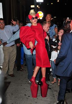 lady in red dress and high heeled boots walking on the street with people behind her