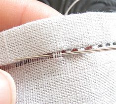 someone is stitching the side of a white piece of fabric with a silver needle