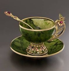 a green cup and saucer sitting on top of a black table next to a spoon