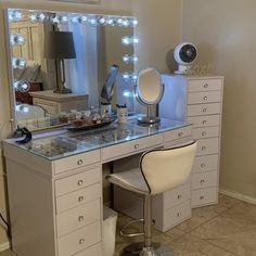 a vanity with lights on it and a chair in front of the mirror that is lit up