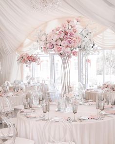 a tall vase filled with lots of pink flowers on top of a table covered in white linens