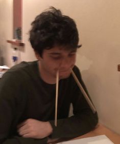 a young man sitting at a table with chopsticks in front of his mouth