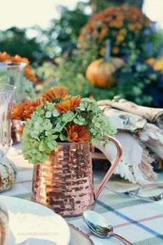 a copper pitcher filled with flowers sitting on top of a table next to plates and utensils