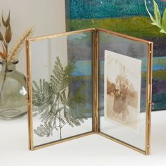 two framed pictures sitting on top of a table next to a vase with flowers in it