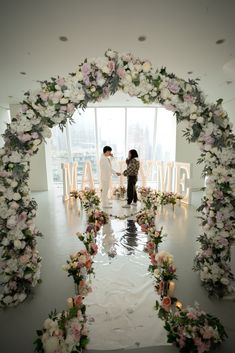 two people standing in front of a floral arch