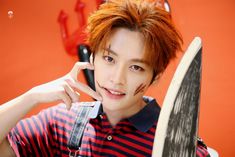 a young man with red hair holding a knife and looking at the camera while standing in front of an orange wall