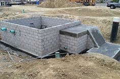 a building under construction in the middle of a dirt field with other buildings behind it