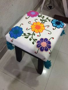 a white stool with colorful flowers painted on the side and tassels around it