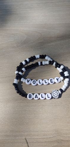 two black and white beaded bracelets with volleyball logos on them sitting on a wooden surface