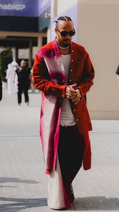 a man with dreadlocks is walking down the street wearing a red and pink coat