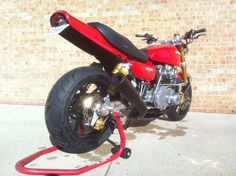 a red motorcycle parked in front of a brick wall with a hose attached to it