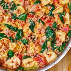 a pizza with spinach, sausage and sauce in a white dish on a wooden table