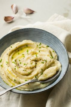 a bowl filled with mashed potatoes on top of a white cloth next to garlic