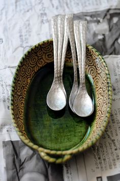 two silver spoons sitting in a green bowl