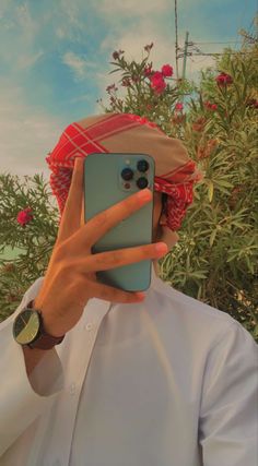 a man taking a selfie with his cell phone in front of some bushes and flowers