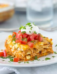 a white plate topped with lasagna covered in sour cream and toppings next to a glass of water