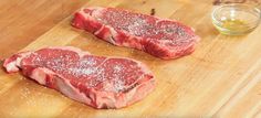 two raw steaks on a cutting board with seasoning