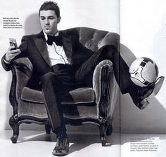 a man in a tuxedo sitting on a chair with a soccer ball and cell phone