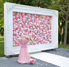 a pink and white wedding backdrop with flowers on the wall, in front of a photo frame