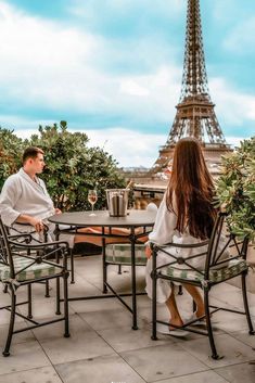 a man and woman sitting at an outdoor table in front of the eiffel tower