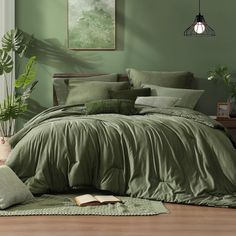 a bed with green sheets and pillows in a room next to a plant on the floor