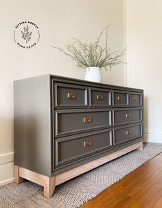 a gray dresser sitting on top of a wooden floor next to a white vase filled with flowers