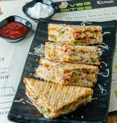 there is a sandwich cut in half on the plate next to some dipping sauces