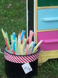 a bucket filled with lots of colorful toothbrushes on top of a green field