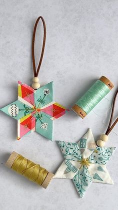 three origami ornaments are hanging from twine spools on a gray surface