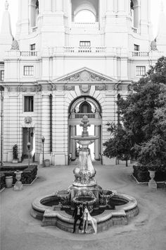 a black and white photo of a fountain in front of a large building with arches