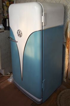 a blue and white refrigerator sitting on top of a wooden floor next to a wall