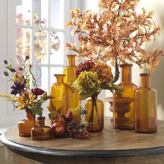 an assortment of vases and flowers on a table in front of a large window