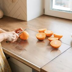 a woman is cutting oranges on a kitchen counter with a knife and some other fruits