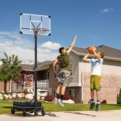 two young men playing basketball in front of a house with a basketball hoop above them