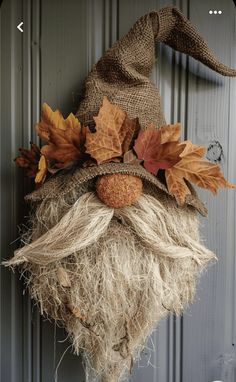 a scarecrow head hanging on the side of a door with autumn leaves and acorns