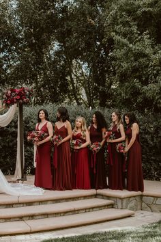 a group of women standing next to each other in front of a wedding arch with flowers on it